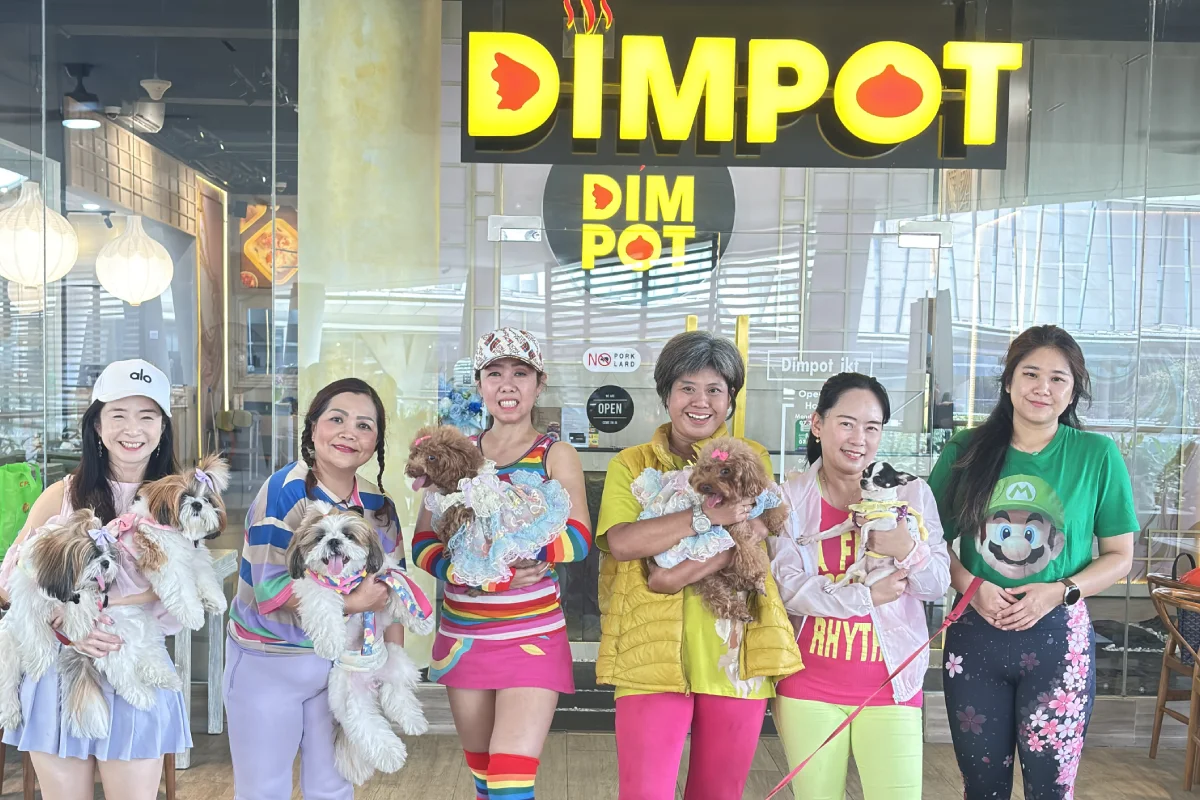 Sekelompok wanita berpose dengan anjing-anjing imut di depan restoran Dimpot, menunjukkan suasana Fun Aerobic with Anabul , yang menggabungkan aktivitas fisik menyenangkan dengan kehadiran hewan peliharaan.